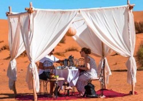 a woman sitting at a table in the desert at Fantastic Luxury Camp in Merzouga
