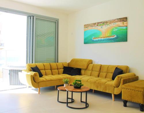 a living room with a yellow couch and a table at Private Jacuzzi, Beach View, Gym, Low Fee For Off-Site Indoor Pool, Spa & Kosher Breakfast ג'קוזי פרטי אם נוף ים, אפשרות לארוחת בוקר כשר, בריכה מקורה, וספא בתשלום ממש מוזל in Ashkelon