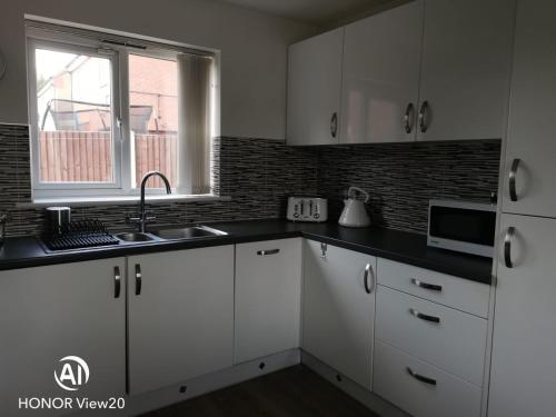 a kitchen with white cabinets and a sink and a microwave at Olive and Carols Walsall Stays in Walsall