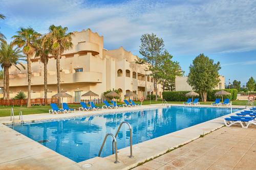 a swimming pool with blue chairs and a building at ALEGRIA Cabo De Gata in Retamar
