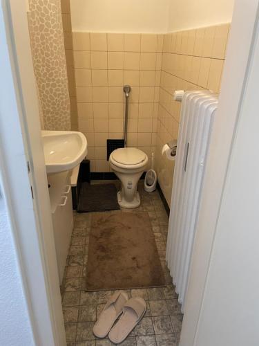 a bathroom with a toilet and a sink and a pair of slippers at SleepWell1 in Cologne