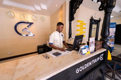 a man standing at a counter with a computer at Golden Tulip Stone Town Boutique in Zanzibar City