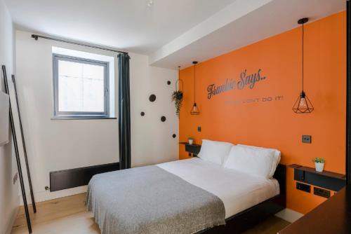 a bedroom with a bed with an orange wall at The Socialite - Covent Garden - by Frankie Says in London