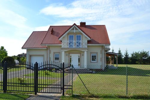 a house with a red roof behind a fence at Domek mamy in Tykocin