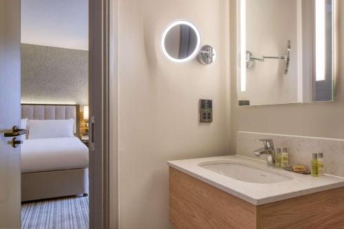 ein Bad mit einem Waschbecken, einem Bett und einem Spiegel in der Unterkunft DoubleTree by Hilton London Chelsea in London