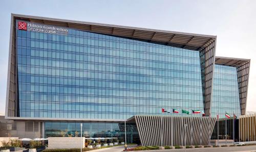 a large glass building with a sign on it at Hilton Garden Inn Kuwait in Kuwait