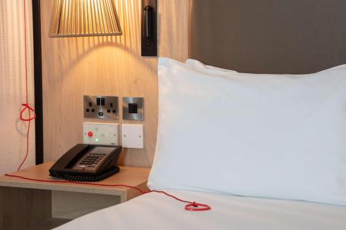 a bed with a pillow and a phone on a table next to a bed at DoubleTree by Hilton London Elstree in Borehamwood