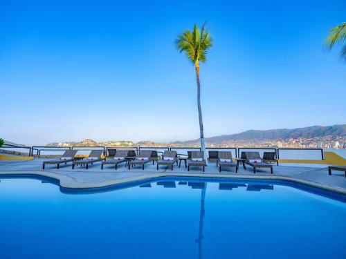 a swimming pool with chairs and a palm tree at Las Brisas Acapulco in Acapulco