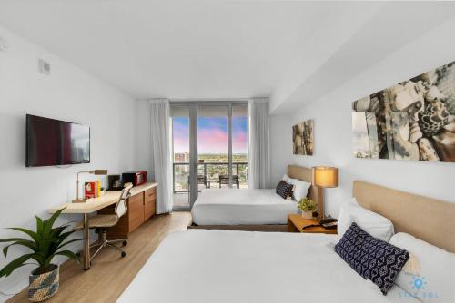 a hotel room with two beds and a desk and a window at Upper studio with Balcony,Pool and Gym, Near Beach in Hallandale Beach