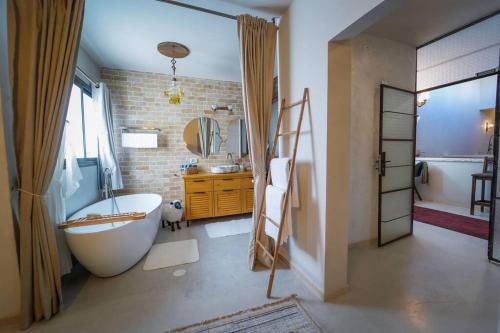 ein Badezimmer mit einer großen weißen Badewanne, einem Waschbecken und einer Badewanne in der Unterkunft Laethos - the house of fun. in Kfar Yona