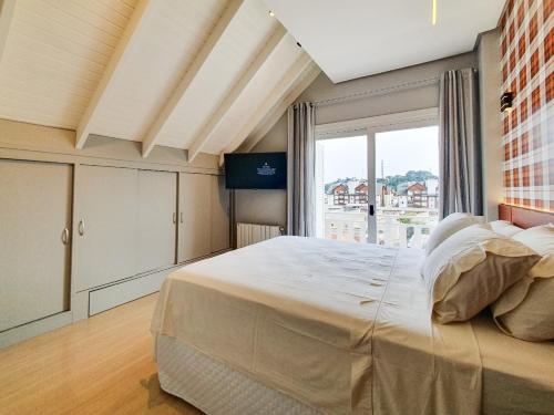 a bedroom with a large bed and a large window at Aconchegante Cobertura no centro de Gramado in Gramado