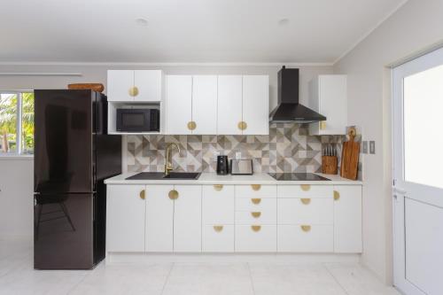 uma cozinha com armários brancos e um frigorífico preto em Studio Varia em Rarotonga