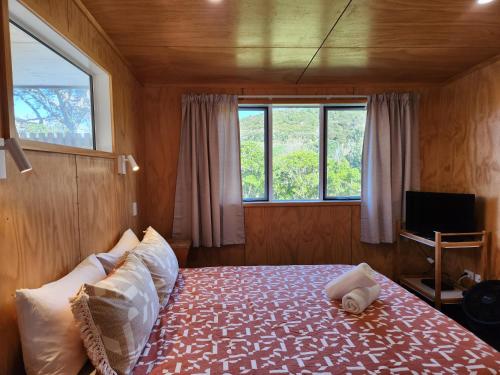 a bedroom with a bed in a room with windows at Tui Nature Retreat in Hotwater Beach
