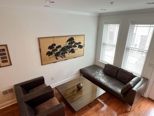 a living room with a black leather couch and two windows at Peaceful Zen Getaway in the City in Philadelphia