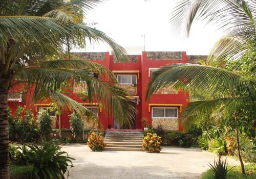 ein rotes Haus mit Palmen davor in der Unterkunft Manasha Apartment 1 in Watamu