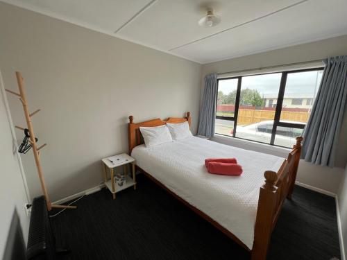 Schlafzimmer mit einem Bett mit einem roten Kissen und einem Fenster in der Unterkunft Yucca Home in Auckland