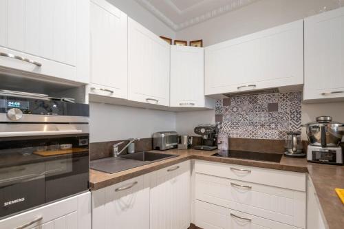 une cuisine avec des armoires blanches et des appareils en acier inoxydable dans l'établissement Appartement de la Coppée - Welkeys, à Paris