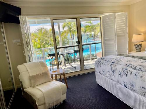 a bedroom with a bed and a chair and a balcony at Oaks Pacific Blue 349 fantastic pool in Salamander Bay