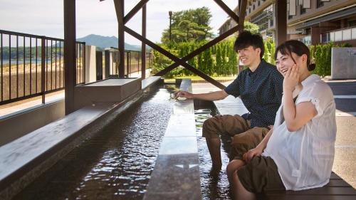 two people sitting on a bench next to a body of water at リゾートホテル美萩 in Hagi