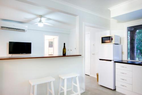 a kitchen with white appliances and two white stools at Airlie Beach Eco Cabins - Adults Only in Airlie Beach