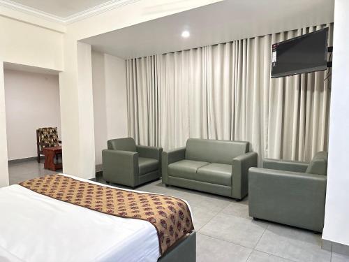 a hotel room with a bed and chairs and a flat screen tv at Nexstay Kassaba Inn in Kozhikode