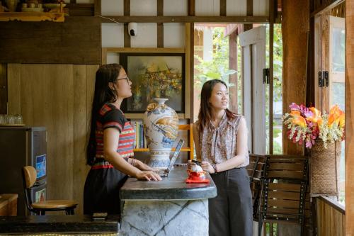 zwei Frauen stehen neben einem Tisch mit einer Vase in der Unterkunft Hue Crown A Luoi Retreat in Ha Tia