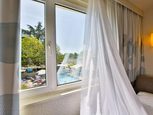 een slaapkamer met een raam met uitzicht op een zwembad bij Novotel Toulouse Purpan Aéroport in Toulouse