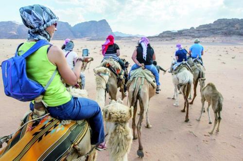 a group of people riding camels in the desert at Mishari Wadi Rum camp in Disah