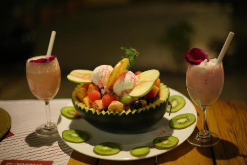 a bowl of fruit on a plate with two cocktails at Monk's Nirvanaa Hotel & Resort in Indore