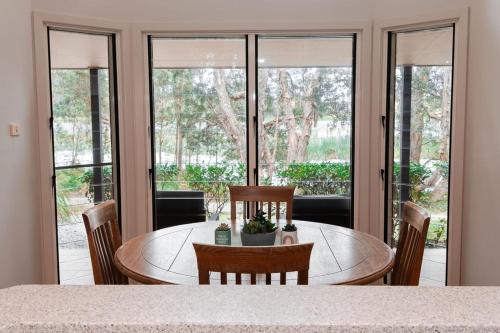 a dining room with a table and chairs and windows at Lake Russell Lakeside Retreat in Emerald Beach