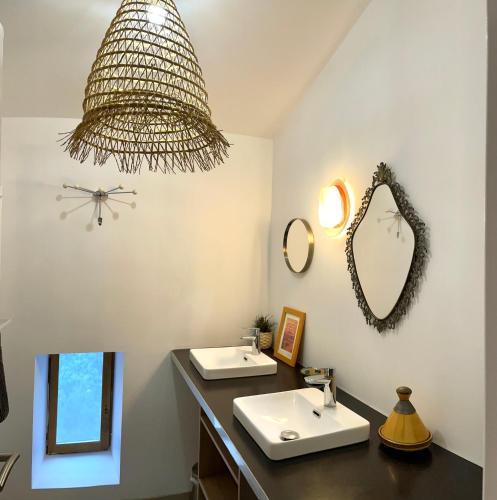 La salle de bains est pourvue de 2 lavabos et d'un lustre. dans l'établissement Les Vignals gîtes et événements Cévennes, à Arphy