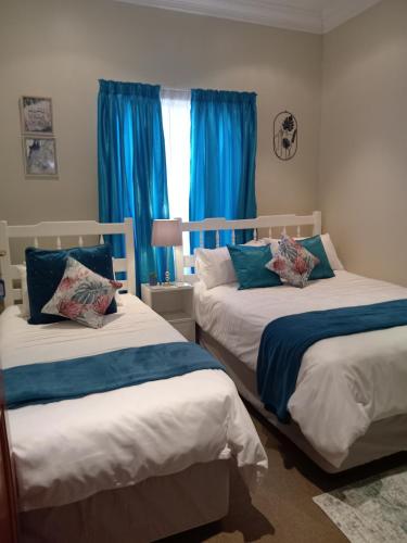 two beds in a bedroom with blue curtains at Fancy Pansy 4: Secure Modern 2 bed family home in Germiston
