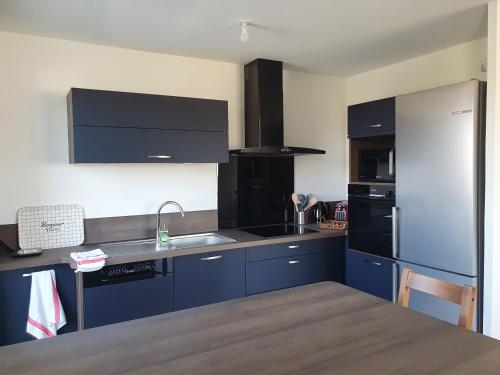 La cuisine est équipée de placards bleus et d'un réfrigérateur en acier inoxydable. dans l'établissement Othello Sea Flat - Appartement terasse familial, à Ouistreham