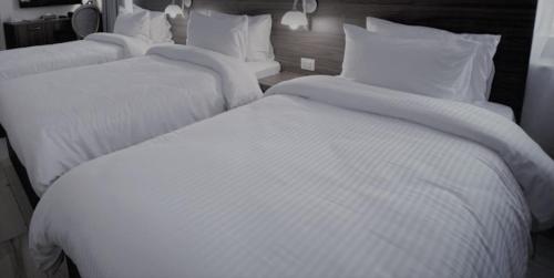 two beds in a hotel room with white sheets and pillows at Petra Gardens in Wadi Musa
