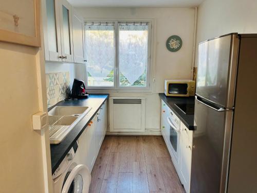 une cuisine avec des armoires blanches et un réfrigérateur en acier inoxydable dans l'établissement Appart T4 côté Dock76 parking, à Rouen