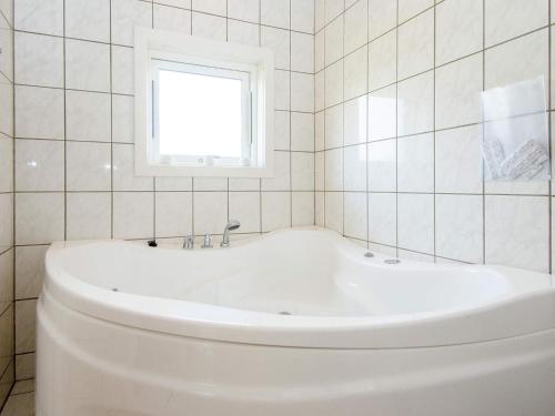 a white tub in a white tiled bathroom with a window at 8 person holiday home in Lemvig in Lemvig
