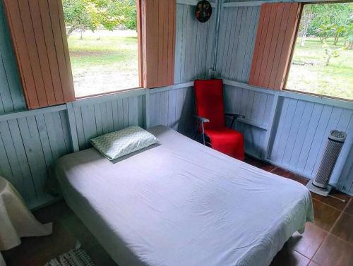 Habitación pequeña con cama y silla roja. en Villa Montezuma Corcovado, en Puerto Jiménez