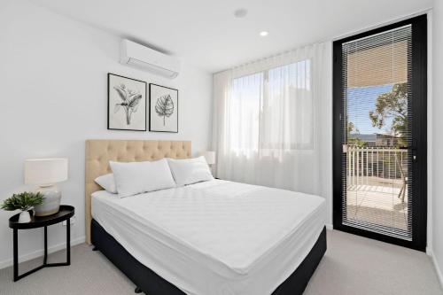 a white bedroom with a large bed and a window at Ohana Apartments 103 in Batemans Bay