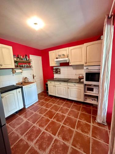 a kitchen with red walls and white cabinets and a tile floor at la maison d'hôtes des Charentes in Les Touches-de-Périgny