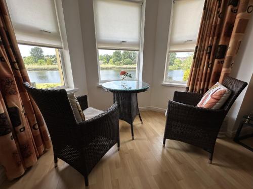 a dining room with chairs and a table and two windows at Coleraine Riverside apartment in Coleraine