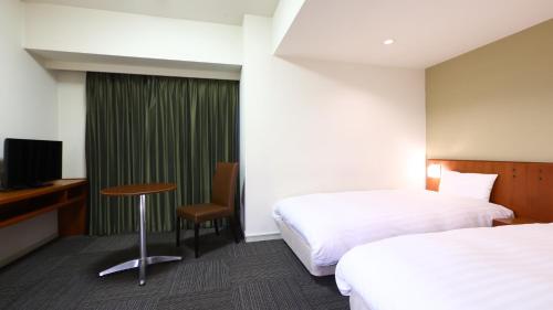 um quarto de hotel com duas camas e uma secretária e uma televisão em Dormy Inn Matsumoto em Matsumoto
