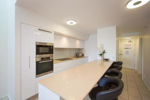 a kitchen with white cabinets and a counter with black chairs at Lanai Riverside Apartments in Mackay