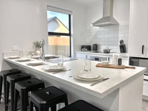 a white kitchen with a counter with stools and plates on it at Villa in Central Hamilton - By KOSH BNB in Hamilton