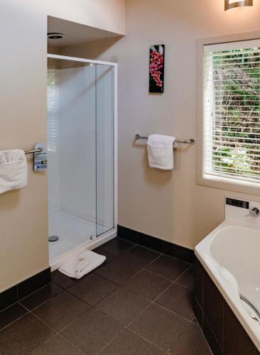 a bathroom with a shower and a tub and a sink at Anchor Lodge Motel in Coromandel Town