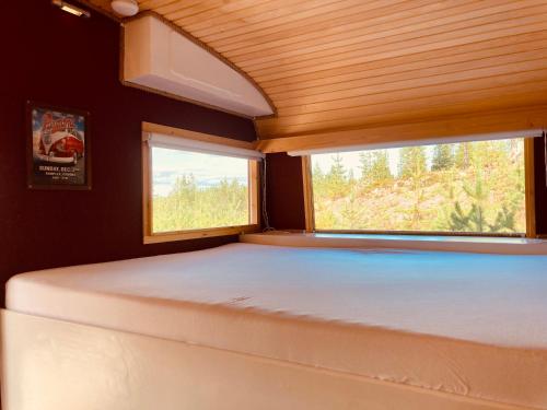 uma cama num pequeno quarto com duas janelas em Offroadcamp em Sörsjön