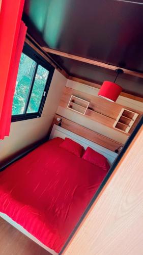 una cama roja en medio de una habitación pequeña en Hébergement insolite dans une clairière, en Beychac-et-Caillau