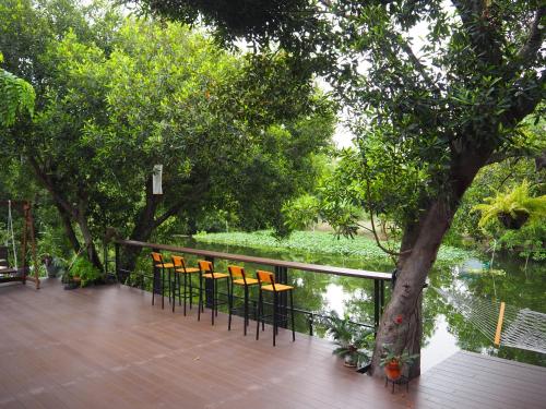 a deck with chairs and a tree and water at Banmai87 Guest House บ้านไม้87 เกสต์เฮ้าส์ in Phra Nakhon Si Ayutthaya