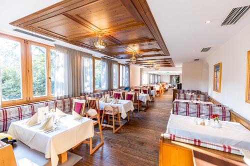 un restaurante con mesas y sillas blancas y ventanas en Das Hopfgarten Familotel Tirol, en Hopfgarten im Brixental