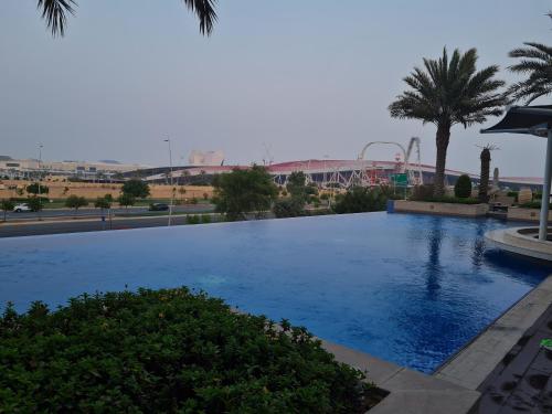 a large blue swimming pool with a roller coaster in the background at Sunset Yas Island Studio near F1 and concerts in Abu Dhabi