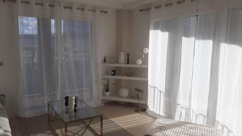 un salon avec des rideaux blancs et une table en verre dans l'établissement Le berlier 13, à Paris